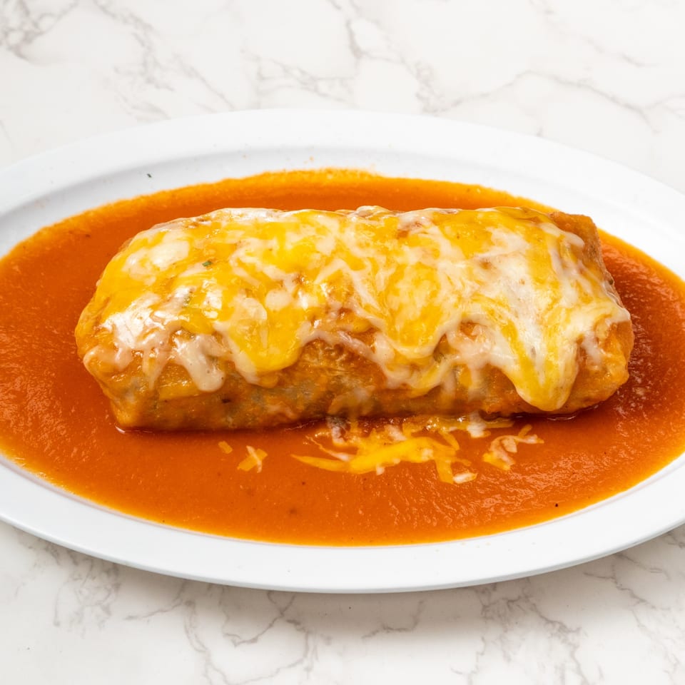 A large, cheesy burrito covered in red sauce on a white oval plate.