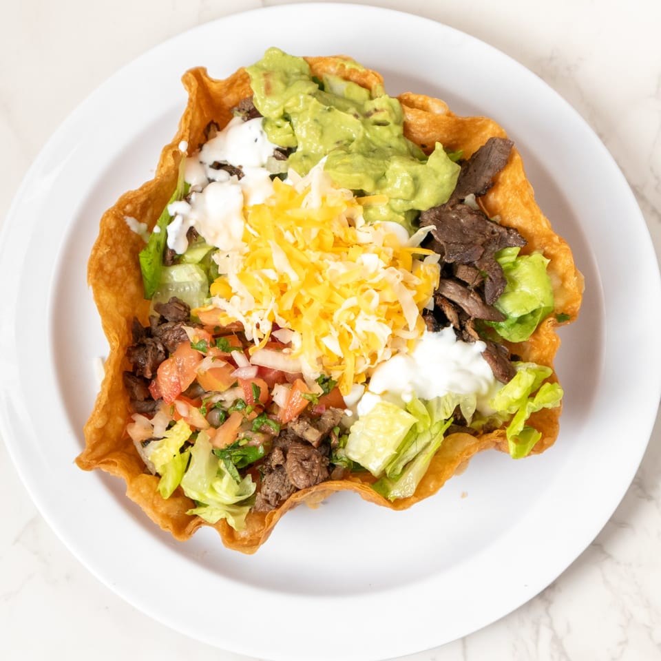 Taco salad in a crispy fried tortilla bowl with beef, lettuce, pico de gallo, cheese, sour cream, and guacamole.