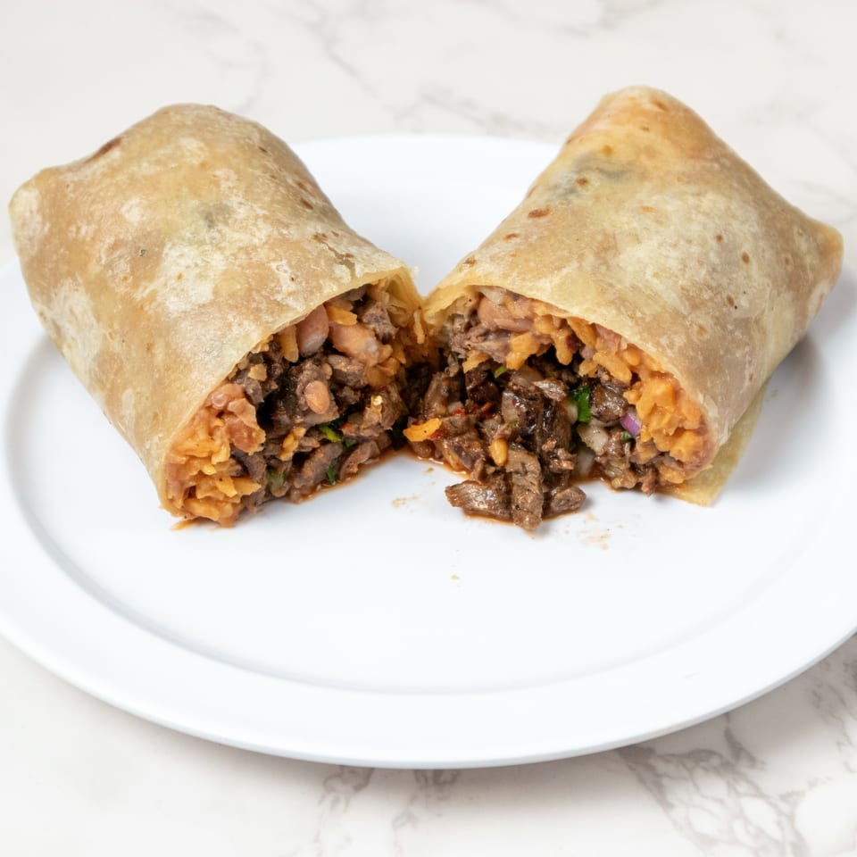 A large burrito, cut in half, revealing a filling of meat, rice, and beans on a white plate.