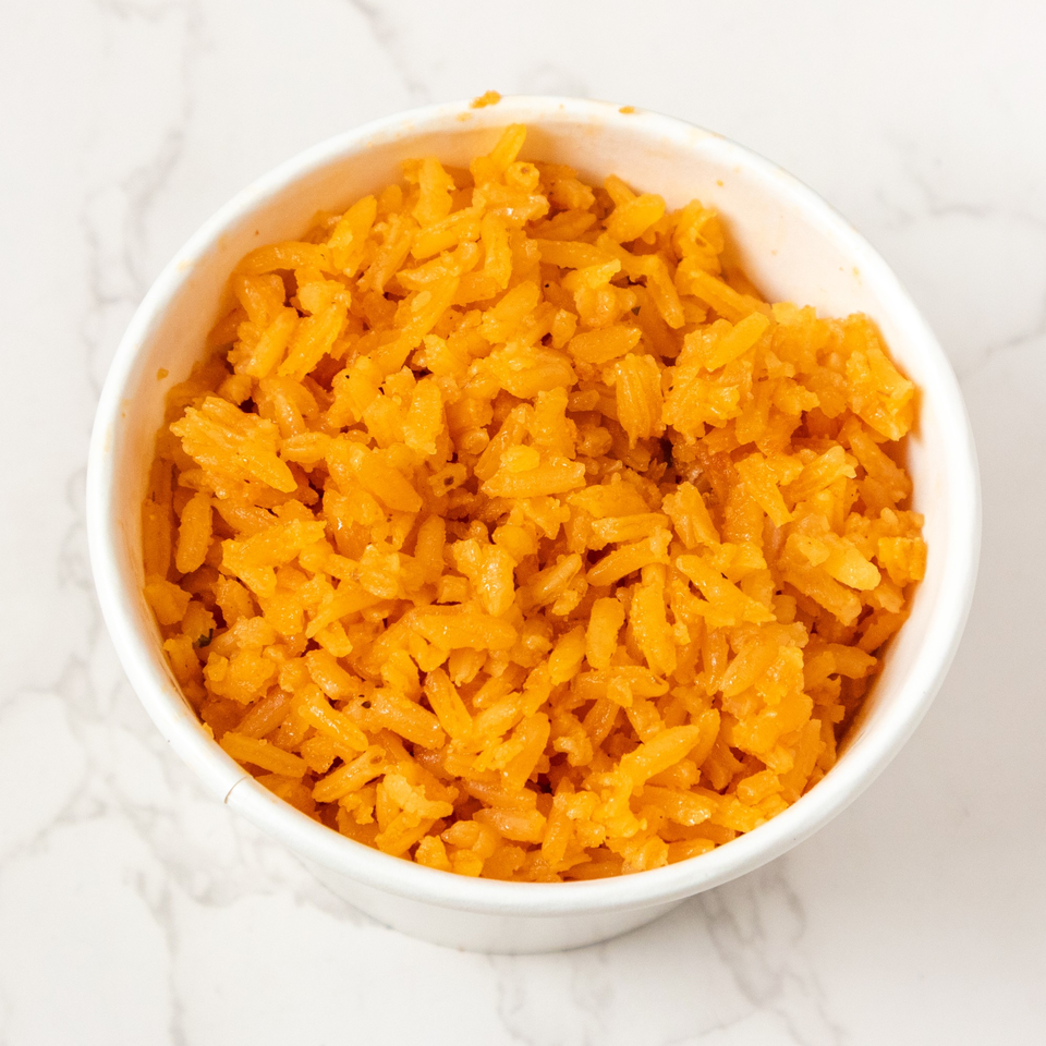A white bowl filled with vibrant orange Mexican rice, on a white marble surface.