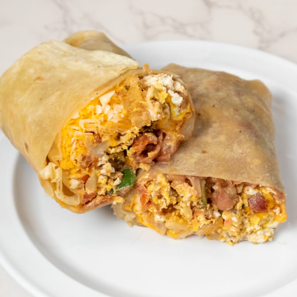A large breakfast burrito, cut in half, filled with scrambled eggs, cheese, and bacon.