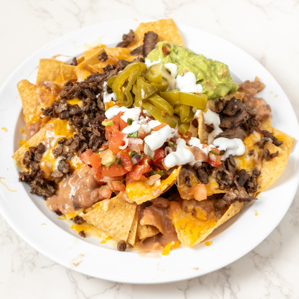 A plate of nachos with steak, refried beans, cheese, pico de gallo, sour cream, guacamole, and jalapeños.