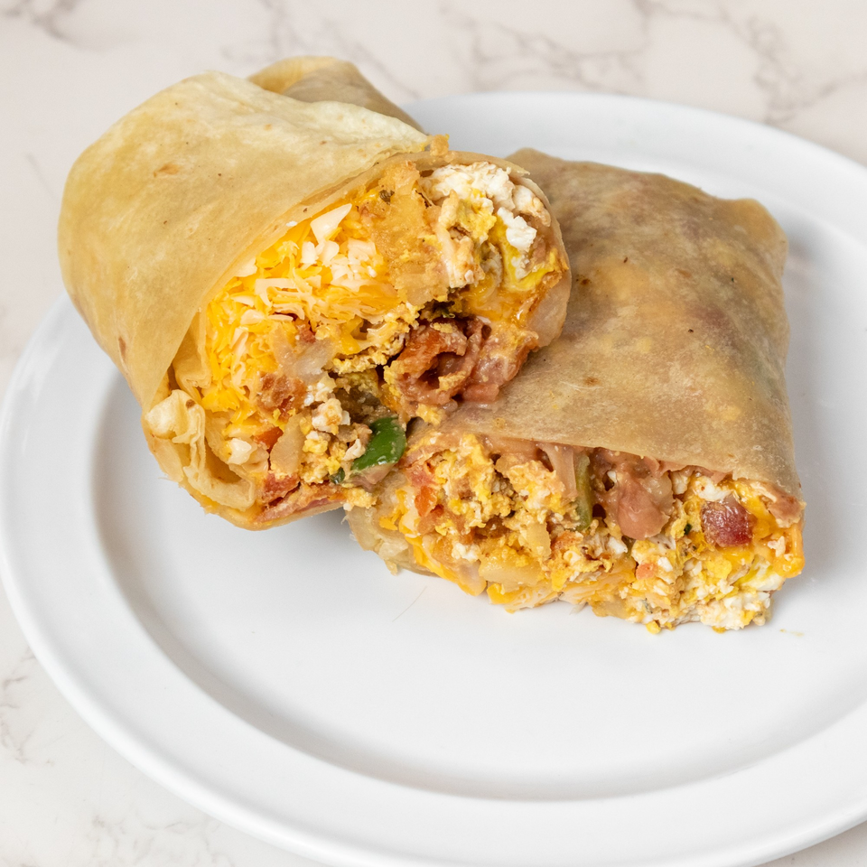 A breakfast burrito, cut in half, revealing scrambled eggs, cheese, and bacon on a white plate.