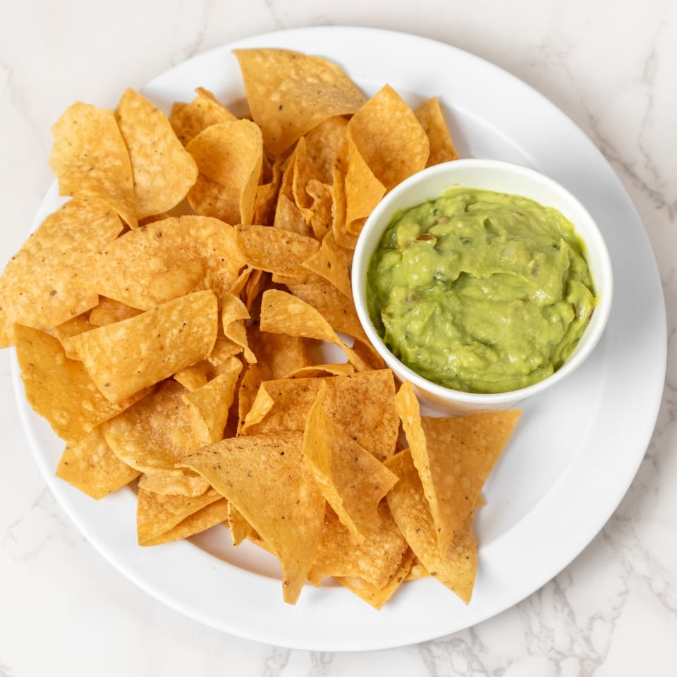 A white plate filled with golden tortilla chips and a small bowl of vibrant green guacamole.
