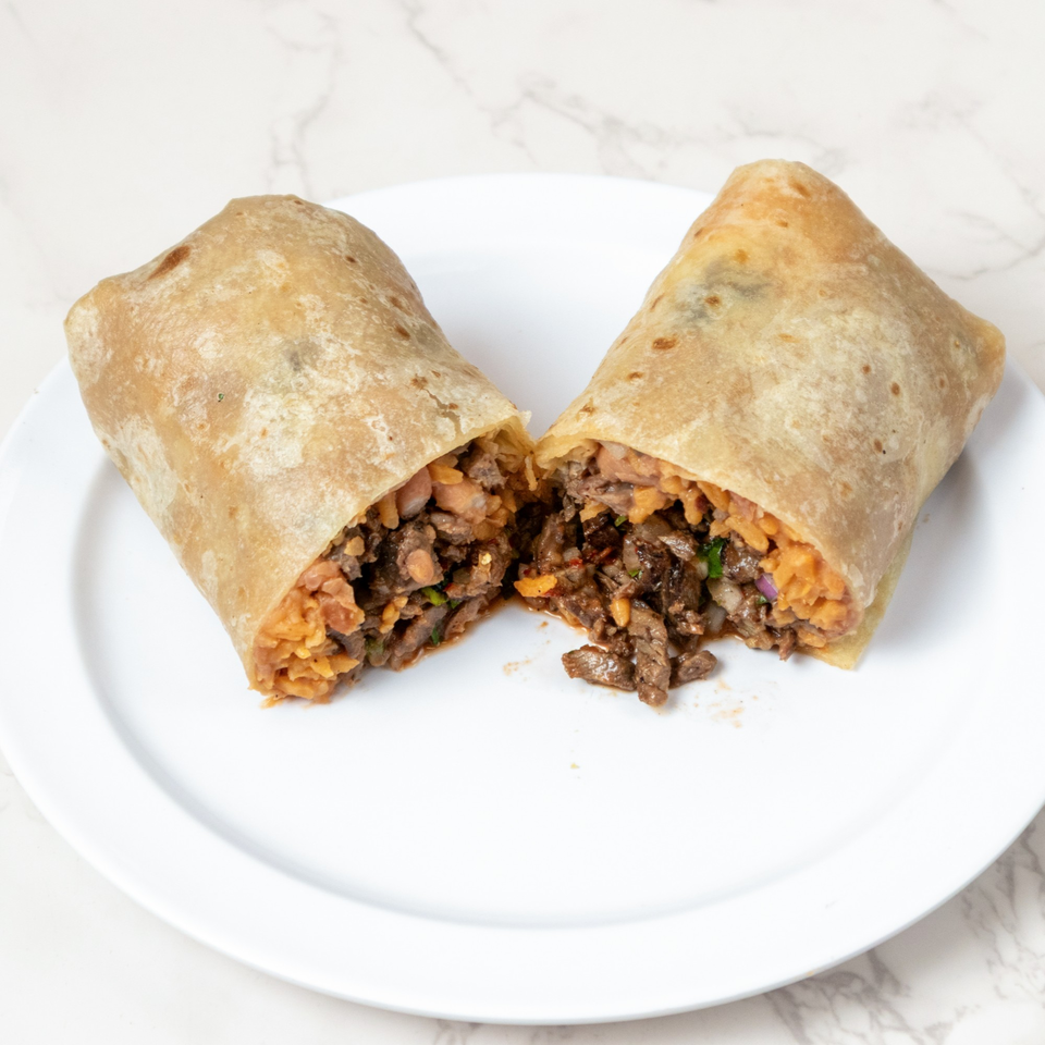 A large burrito, cut in half, revealing steak, rice, and beans on a white plate.