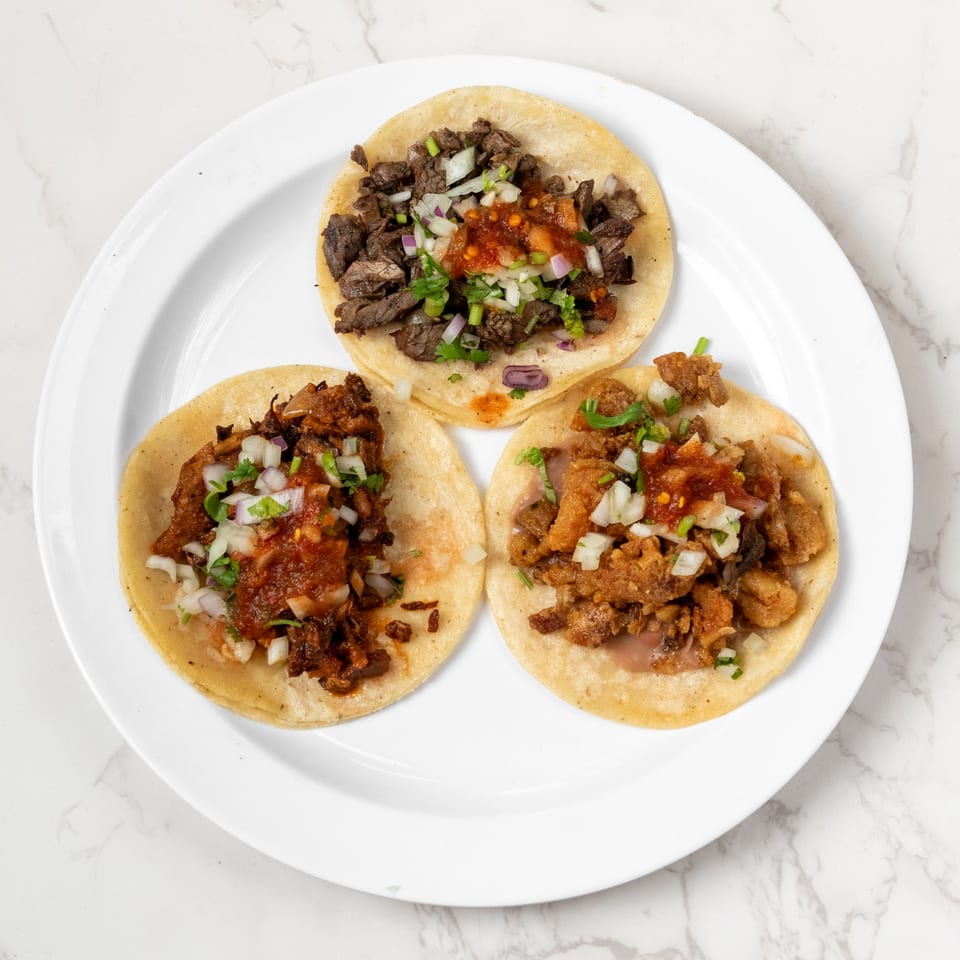 Three tacos with different meat fillings, salsa, and diced onions on a white plate.