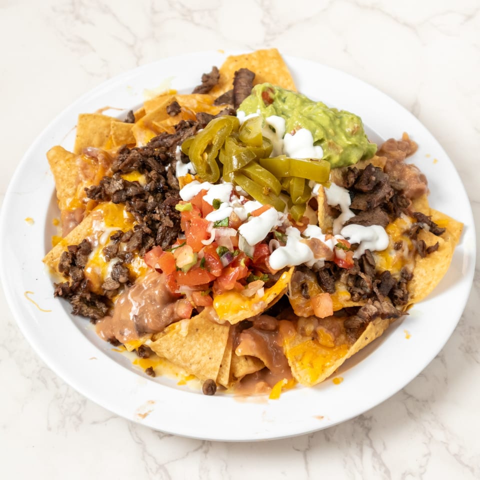 A plate of nachos with steak, refried beans, cheese, guacamole, jalapeños, and pico de gallo.