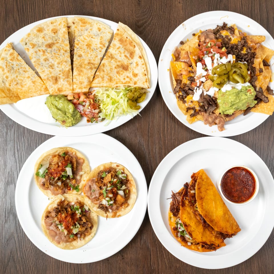 Four white plates of Mexican food: quesadillas, nachos, street tacos, and birria tacos with consommé.
