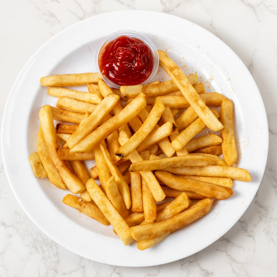 Golden french fries with a side of ketchup on a white plate, against a marble background.