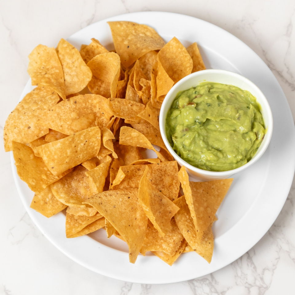 A white plate filled with golden tortilla chips and a small bowl of green guacamole.